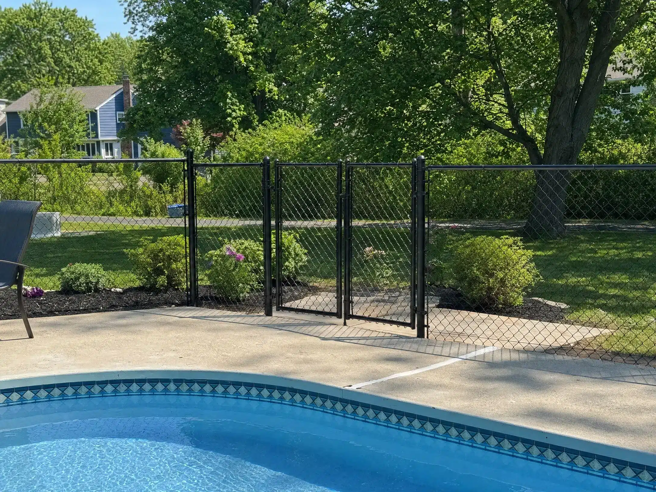 Black vinyl-coated chain-link pool fence with a double safety gate enclosing a residential swimming pool.