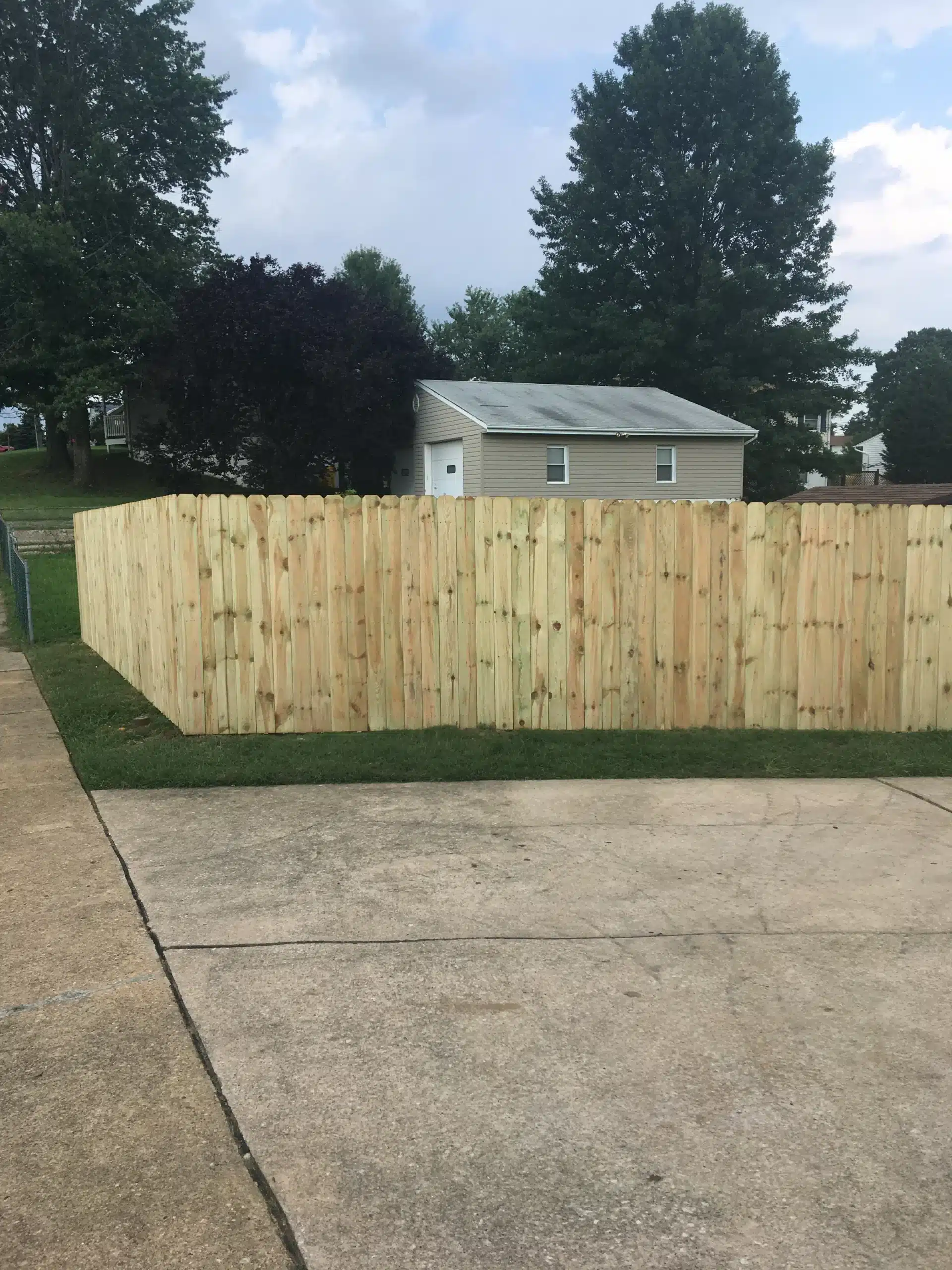 Pressure-treated dog-ear wood privacy fence installed beside a concrete driveway in Pasadena, MD.