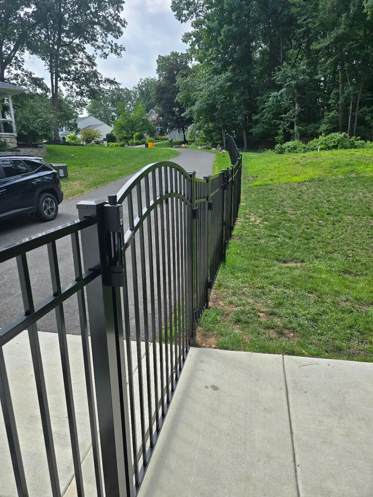 Close-up view of a black aluminum gate and fence installed beside a driveway in Pasadena, MD.