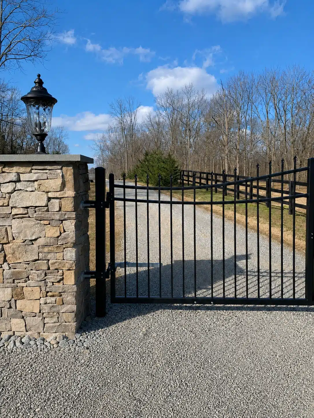 Automated black metal swing gate installed at a gravel driveway entrance in Severna Park.