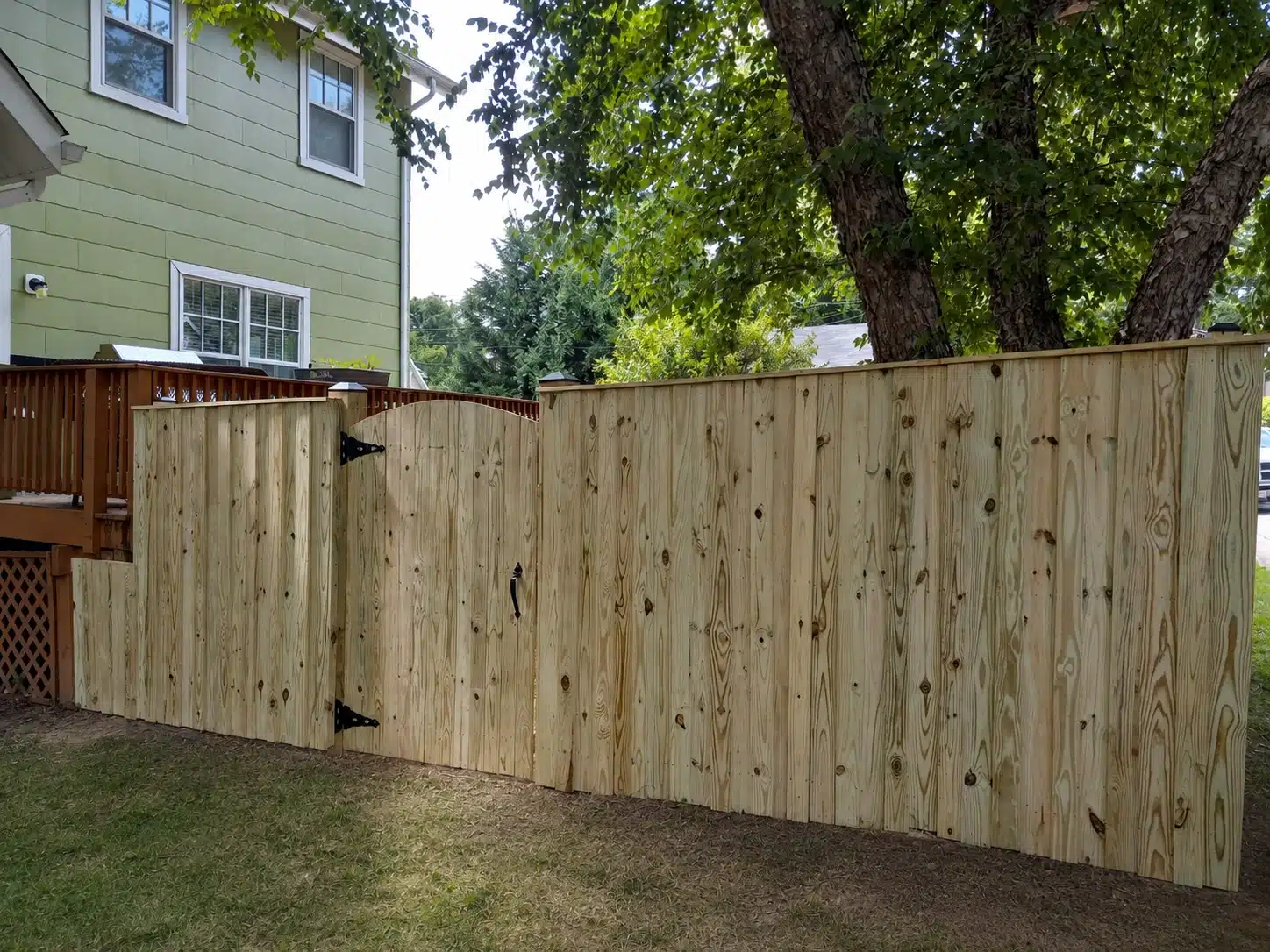 Board-on-board wood privacy fence with a matching arched gate beside a backyard deck in Pasadena, MD.