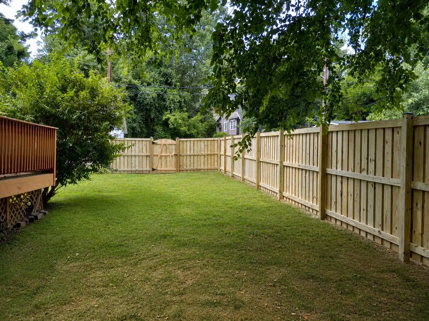 Board-on-board wood fence enclosing a shaded backyard with a matching gate in Pasadena, MD.
