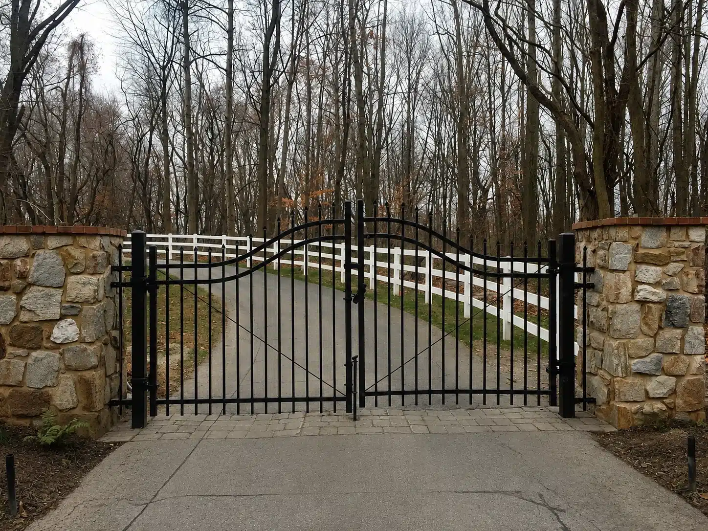 Wrought iron driveway gate between stone pillars on a wooded property in Severna Park, MD.