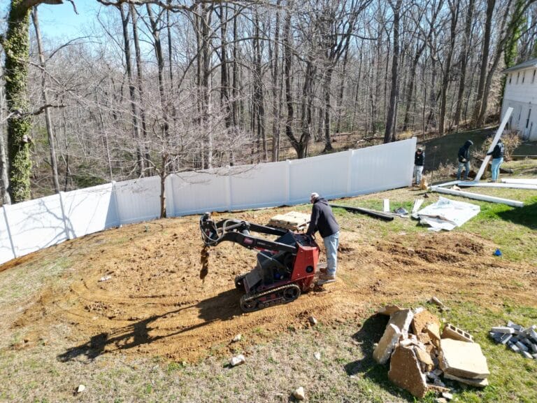 a man working near white privacy fence near trees
