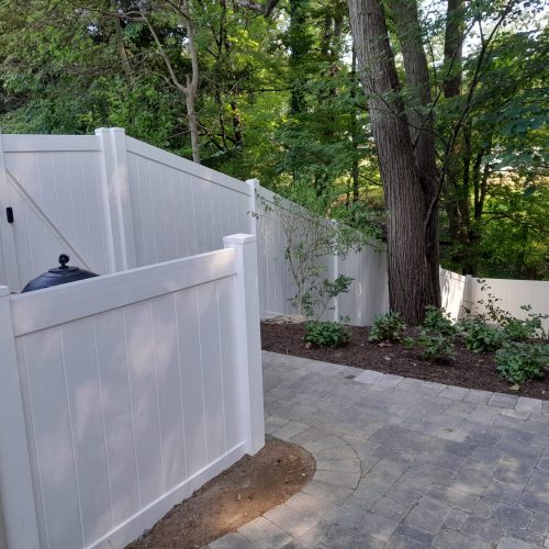 sloped white vinyl privacy fence near a tree