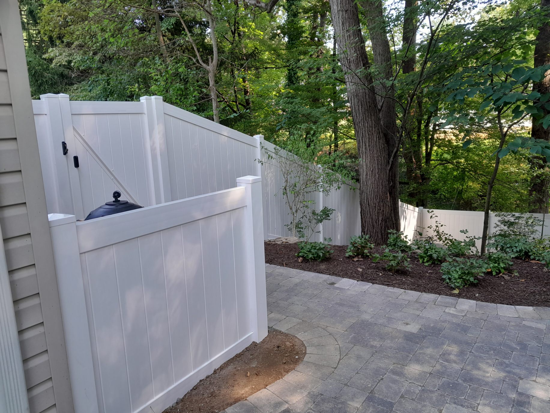 sloped white vinyl privacy fence near a tree