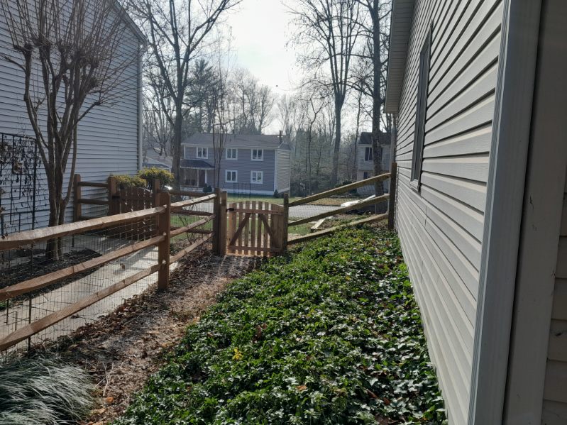 Welded wire reinforced split-rail fence enclosing a side yard with gravel path in Crownsville, MD
