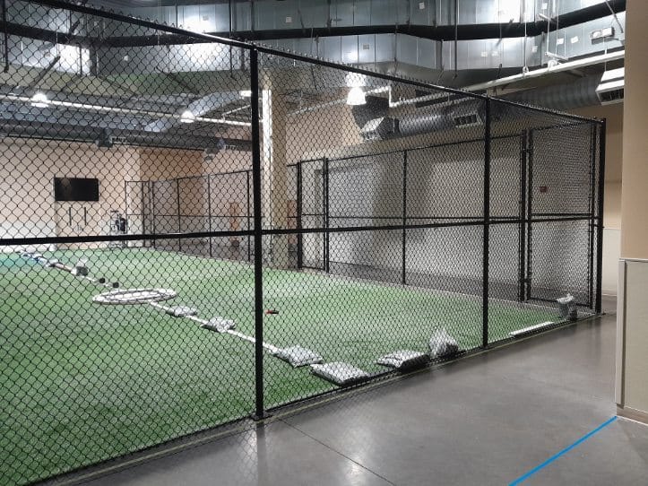 Tall black chain-link fencing separating indoor activity zones in a Crofton training building