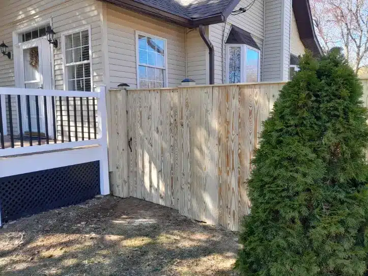 Vertical board wood fence beside tan house and porch