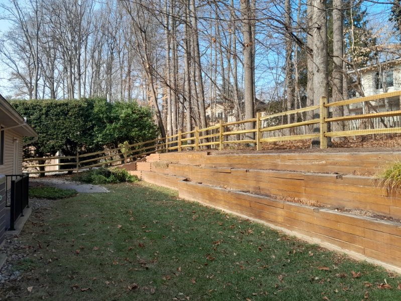Three-rail split-rail fence bordering terraced wooden retaining walls in a Crownsville backyard