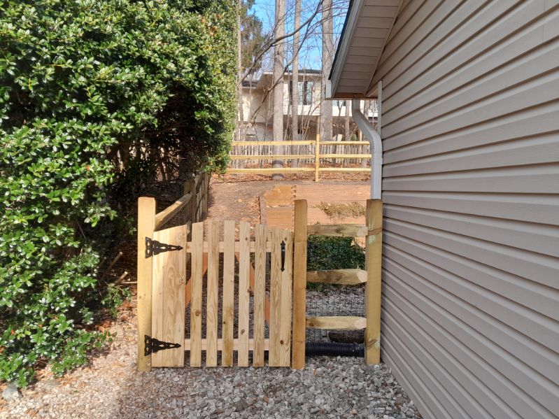 Wooden three-rail split-rail fence running along a landscaped slope in Crownsville, Maryland