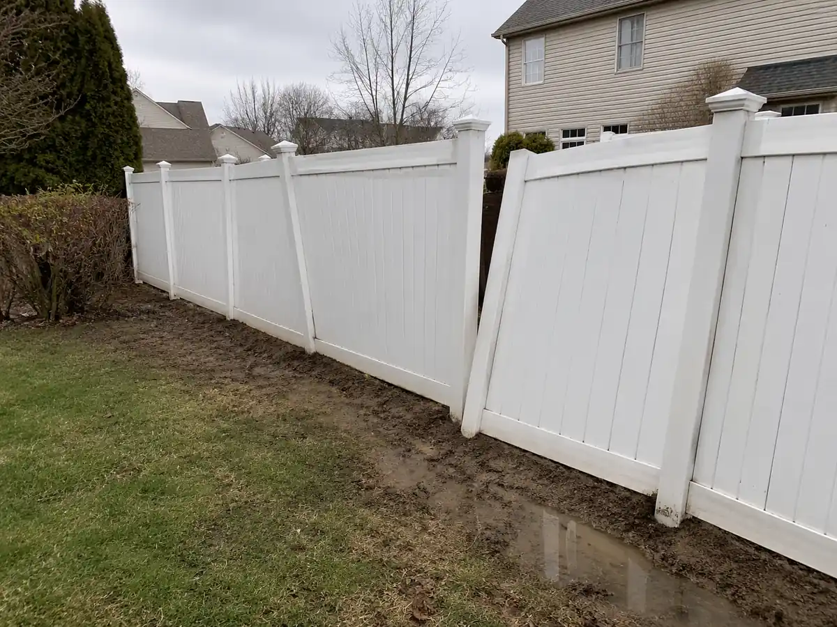 Leaning white vinyl fence in a muddy Maryland backyard showing problems from improper installation