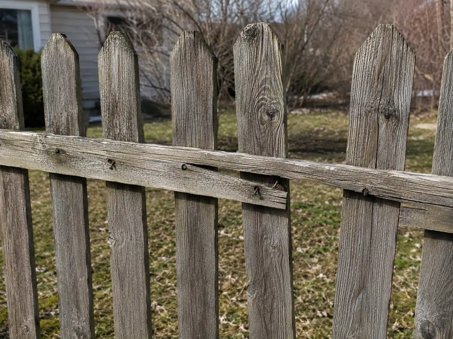 Weathered wood fence with separated pickets and a loose rail in Pasadena, MD, showing damage that should be repaired during spring maintenance.