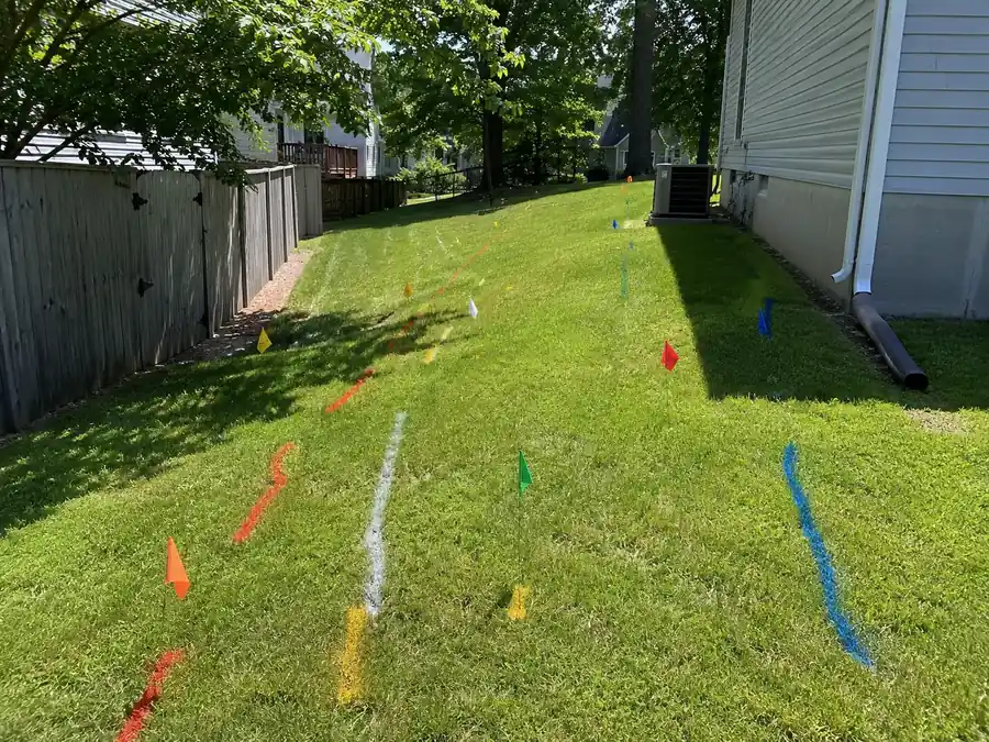 Utility markings and colored flags in a Glen Burnie yard before wood fence installation.