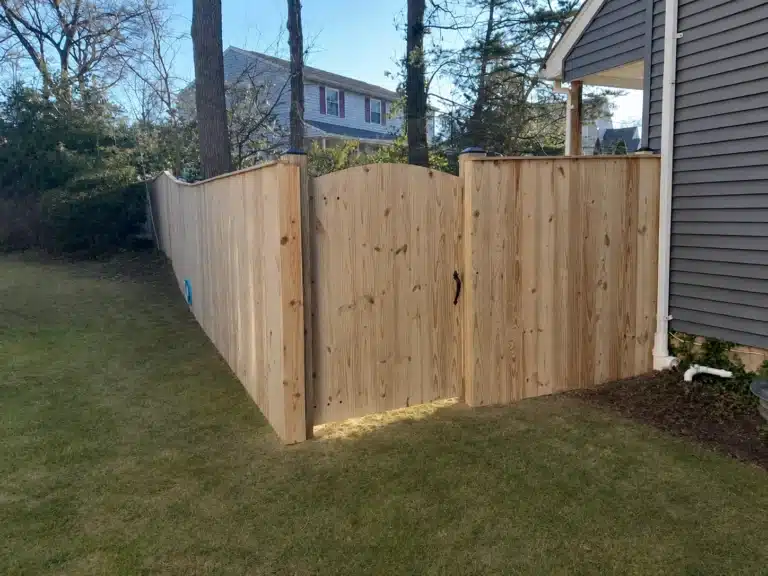 Pressure-treated scalloped privacy fence with a matching wood gate beside a home in Pasadena, MD.