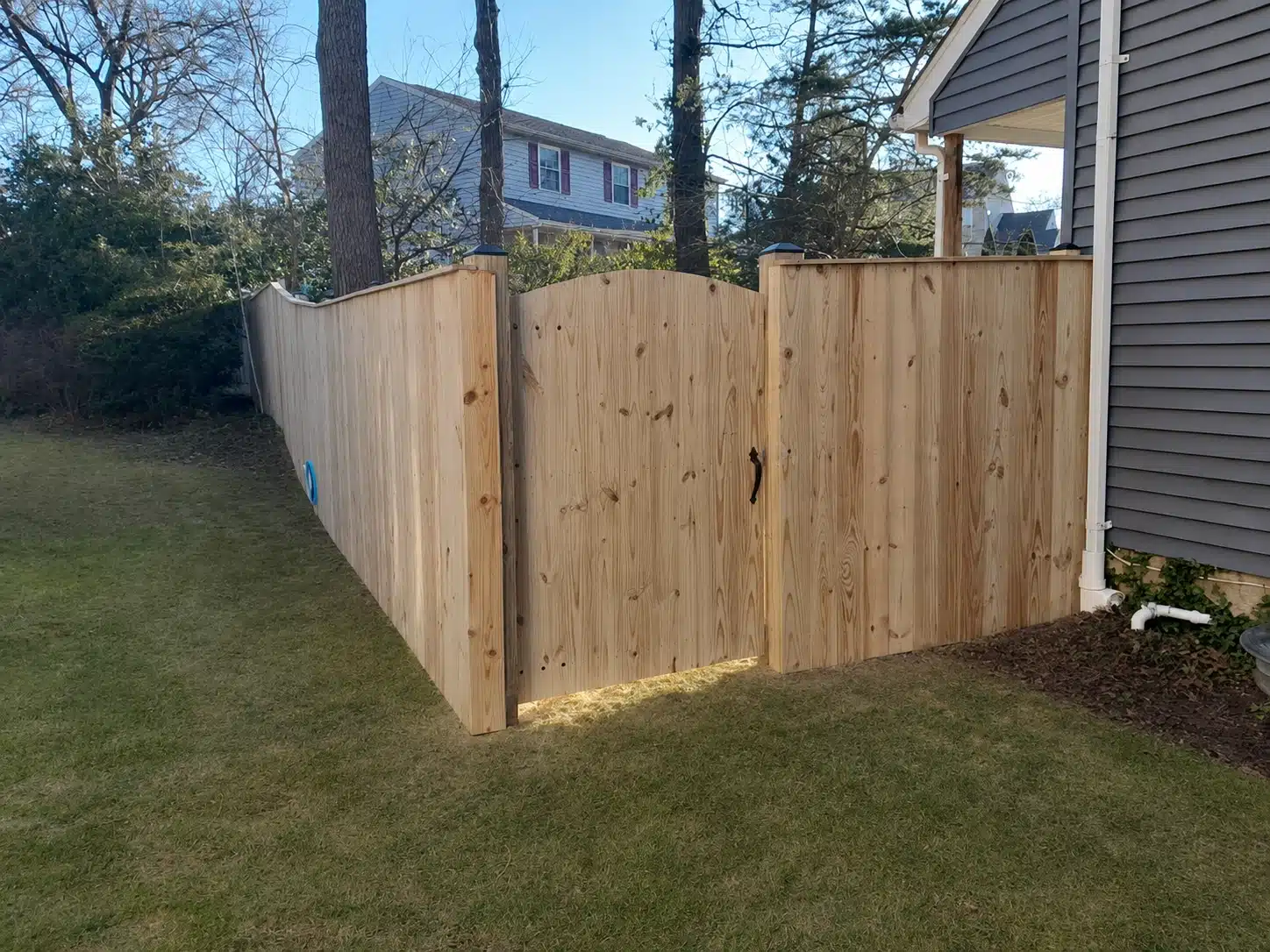 Pressure-treated scalloped privacy fence with a matching wood gate beside a home in Pasadena, MD.