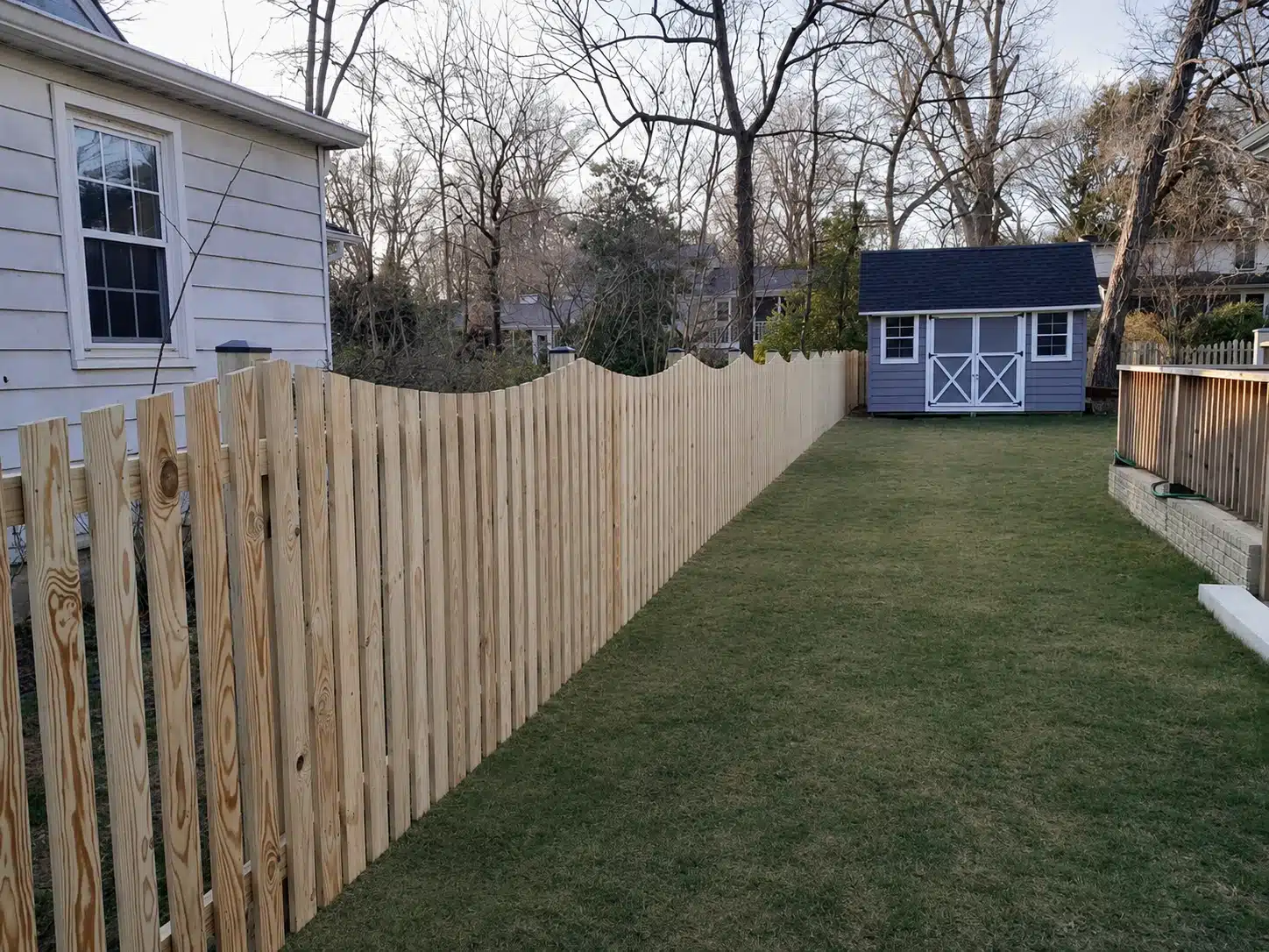 Pressure-treated scalloped spaced picket fence running through a narrow side yard in Pasadena, MD.