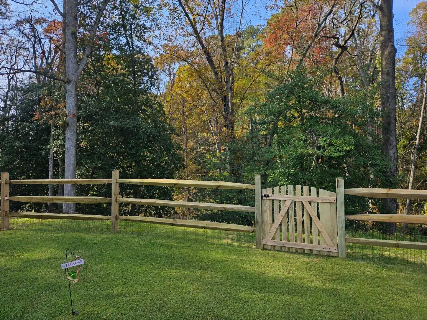 Split rail fence with wire mesh and a wood gate bordering a wooded backyard in Anne Arundel County, MD.