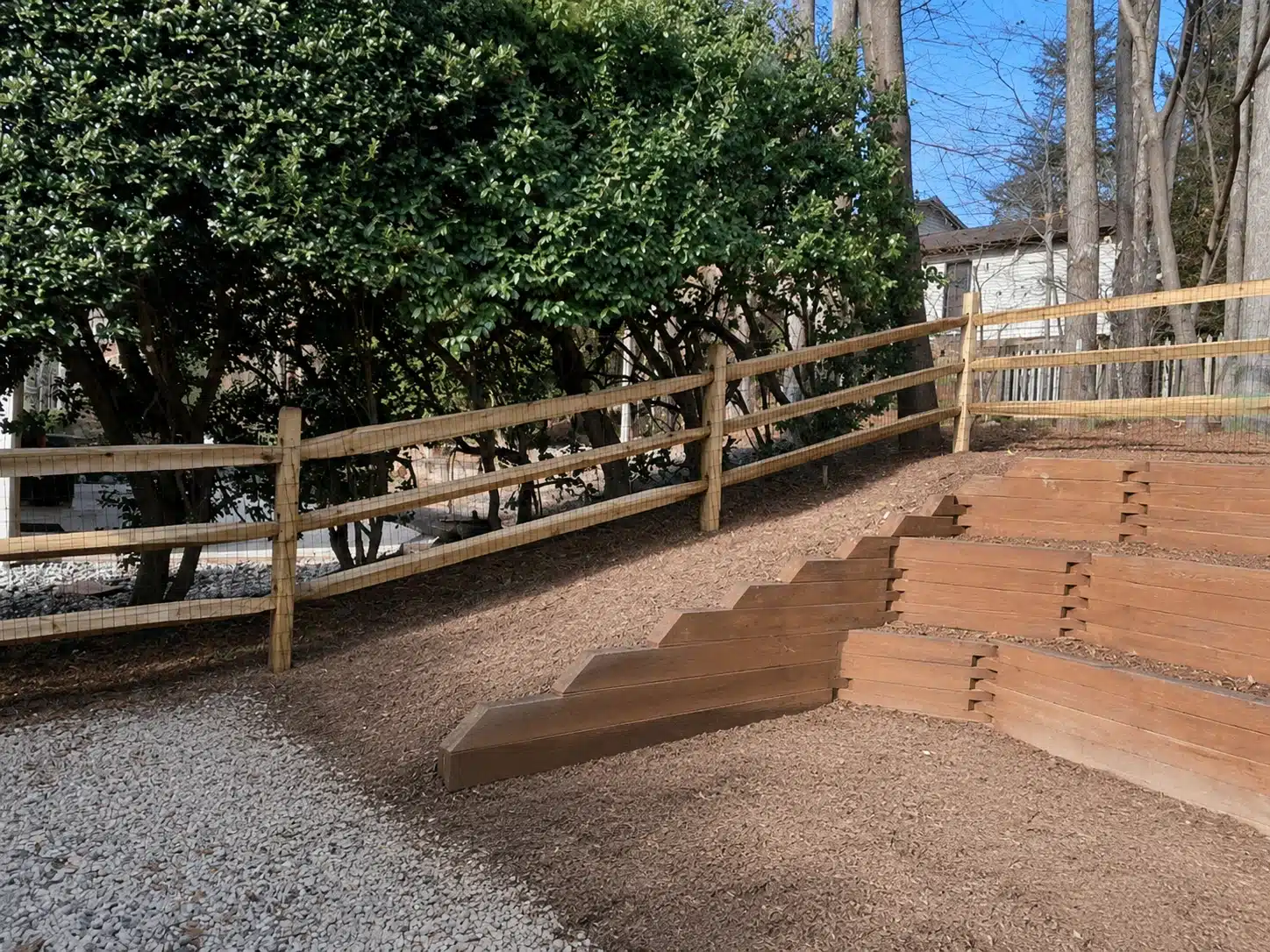 Split rail fence installed above a tiered retaining wall on a sloped property in Anne Arundel County, MD.