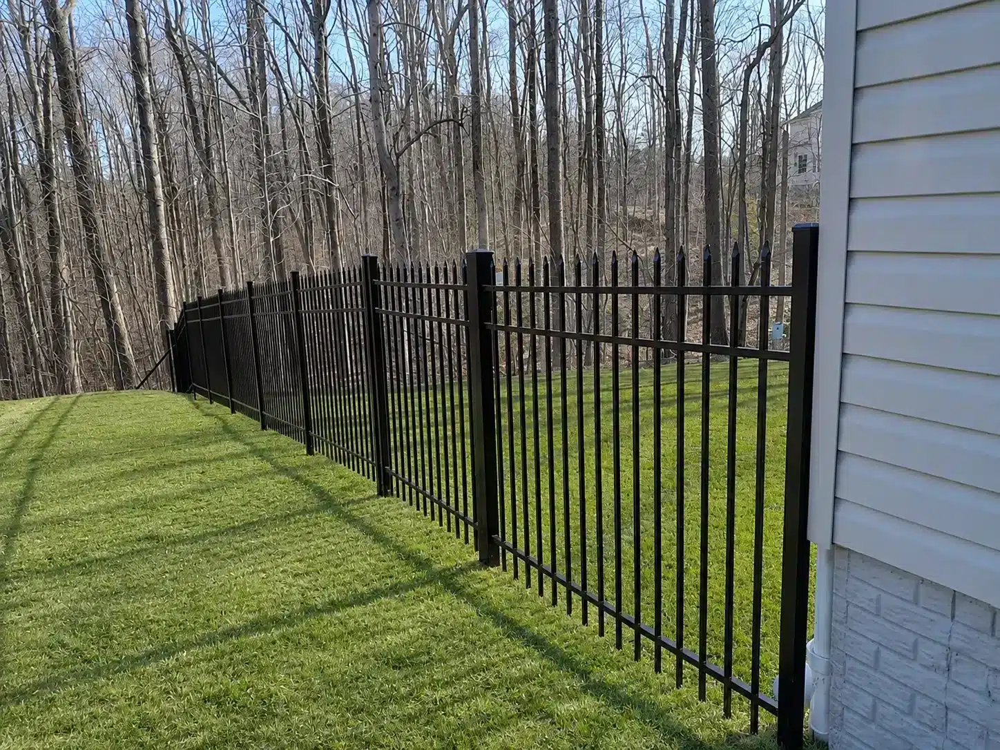 Decorative black steel fence installed around a residential yard in Maryland with wooded surroundings.