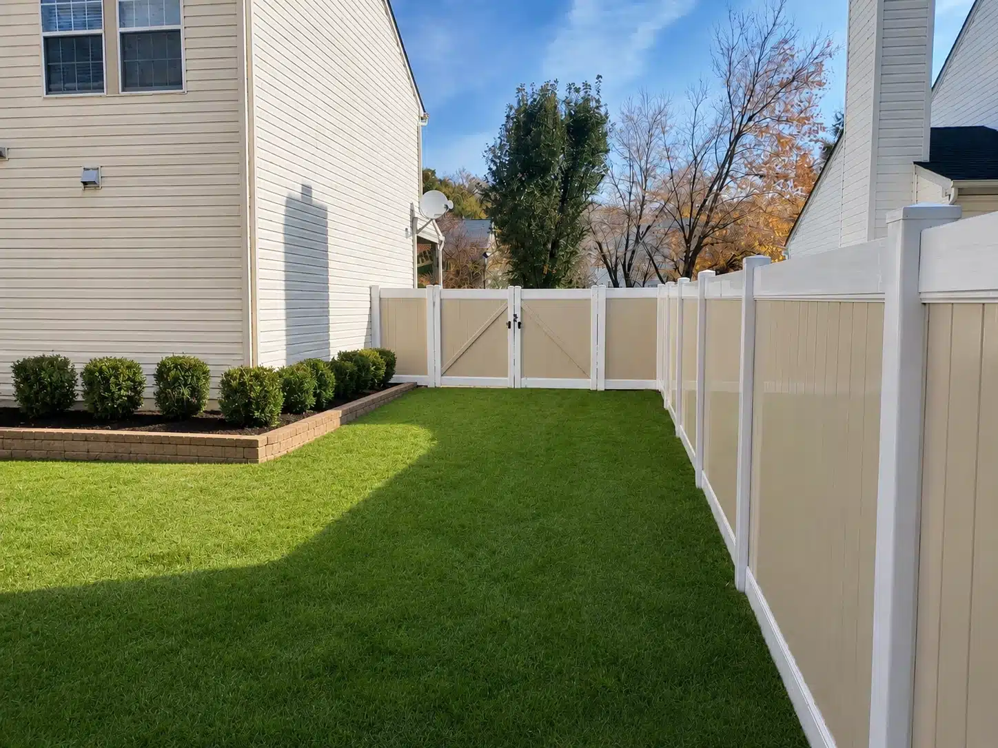 Tan and white vinyl fence double gate with privacy panels along a residential backyard.