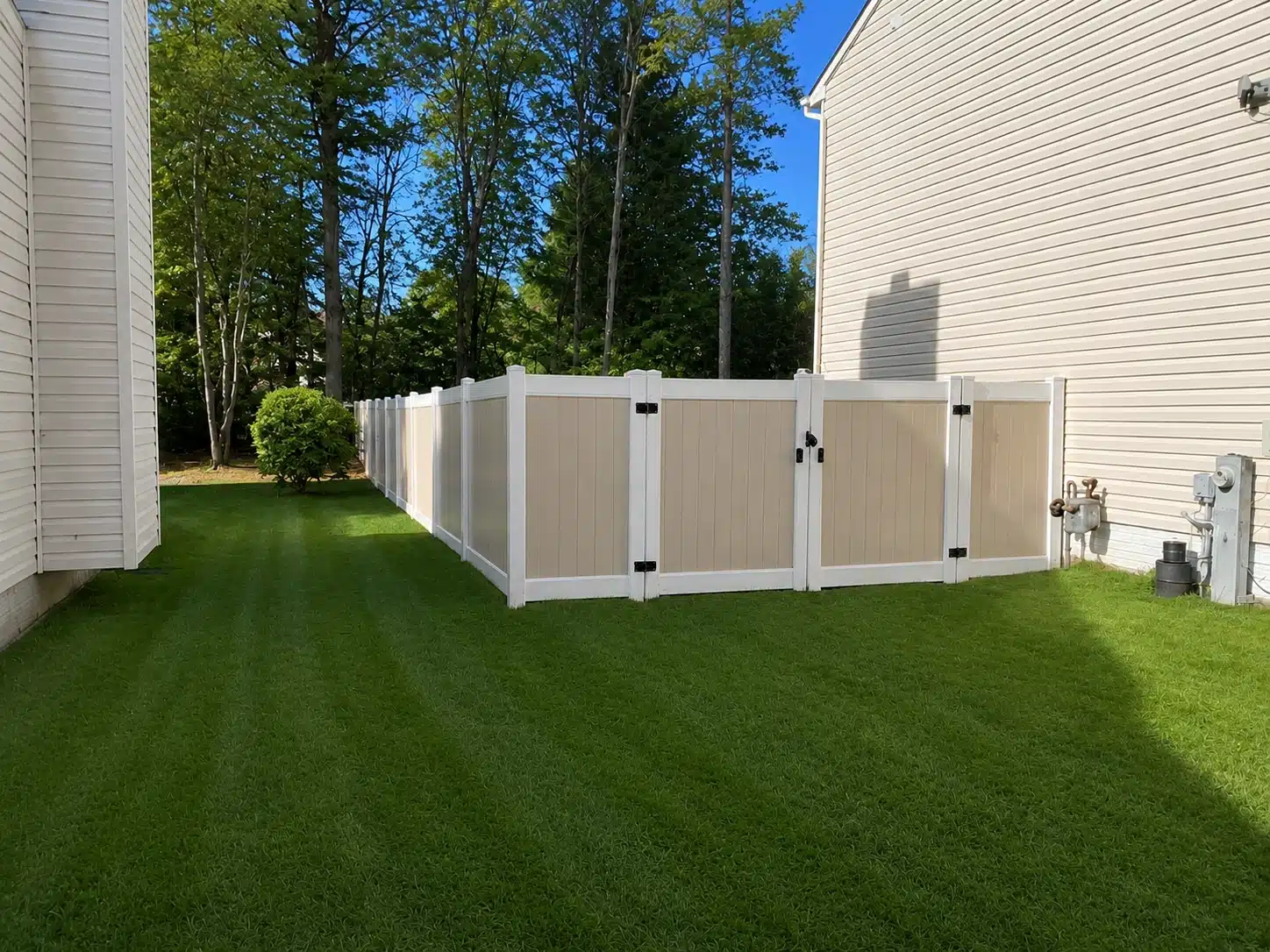 Vinyl privacy fence installation in Harlan IN — tan and white fence panels with double gate enclosing a clean side yard.