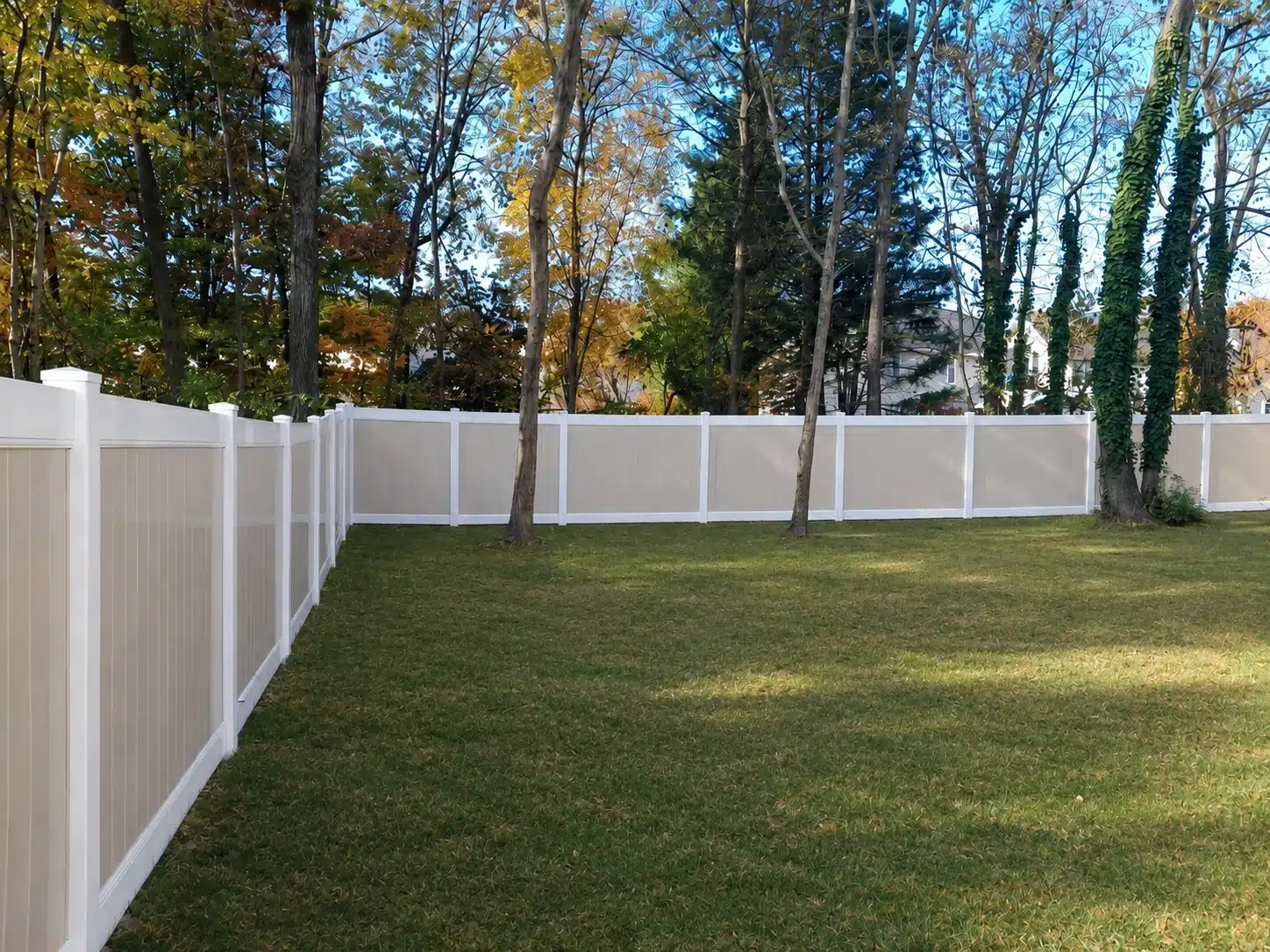 Two-tone tan and white vinyl privacy fence enclosing a spacious wooded backyard in Odenton, MD.