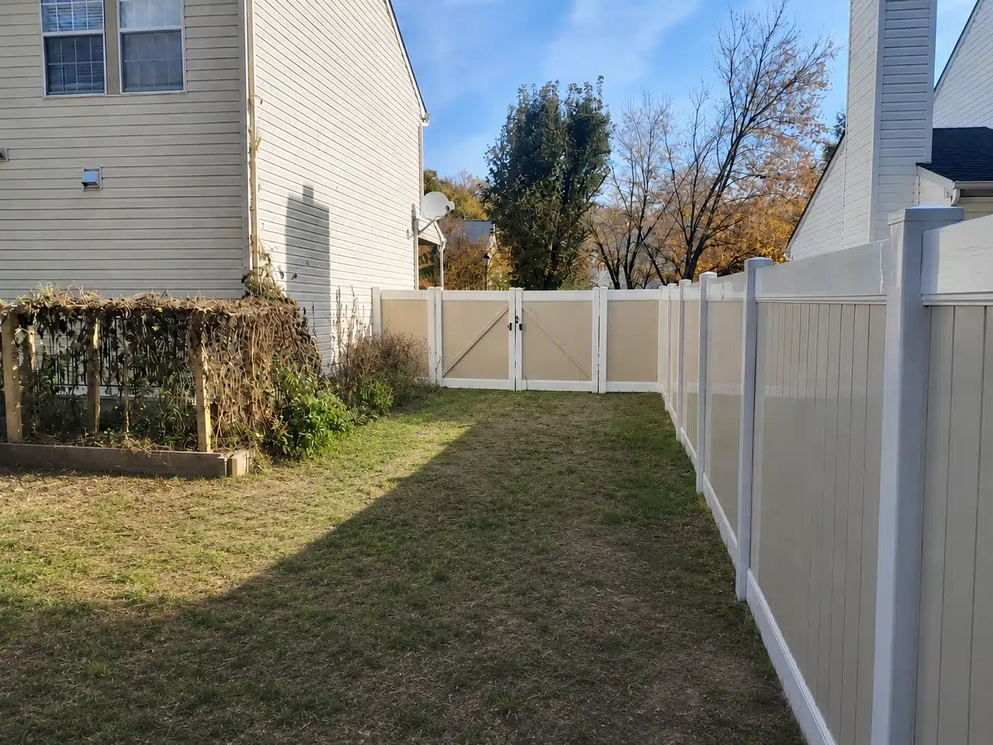 Two-tone vinyl privacy fence with a double gate enclosing a side yard in Odenton, MD.