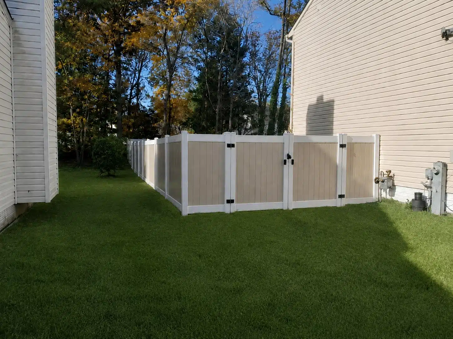 Tan and white vinyl privacy fence with gate panels installed between homes in Odenton, MD.