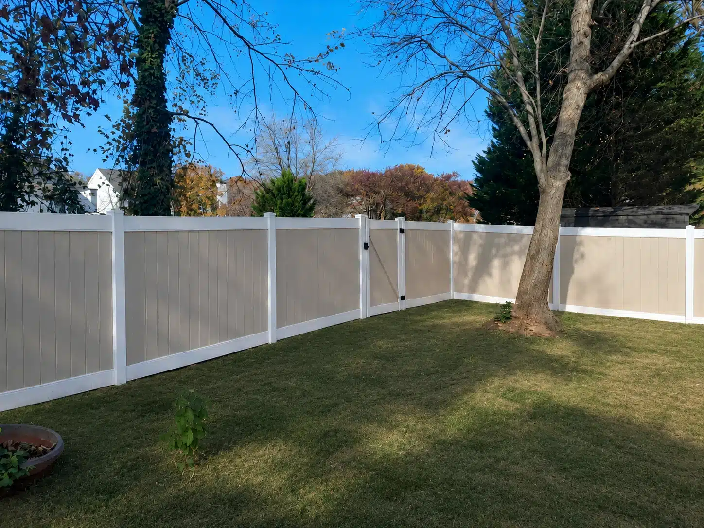 Wide backyard enclosed by a tan and white vinyl privacy fence with mature trees in Odenton, MD.