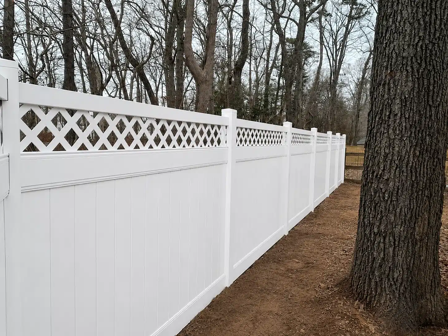 White decorative vinyl privacy fence with lattice-top panels installed around a wooded yard in Severna Park, MD.
