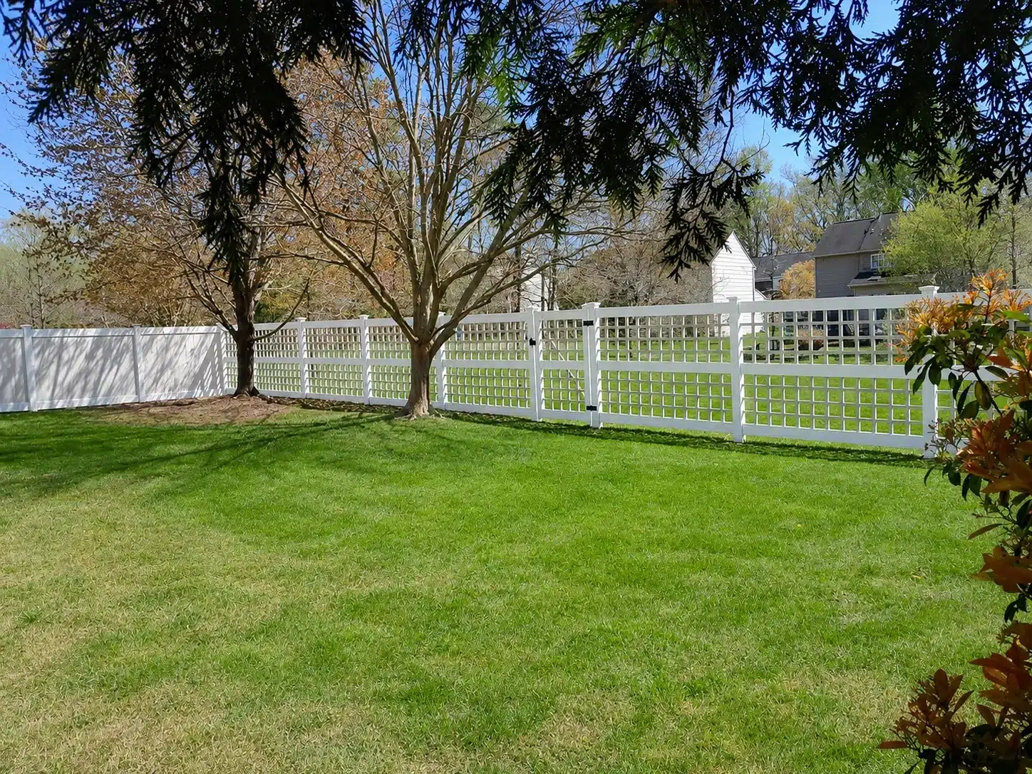 White decorative open-lattice vinyl fence installed across a landscaped backyard in Severna Park, MD.