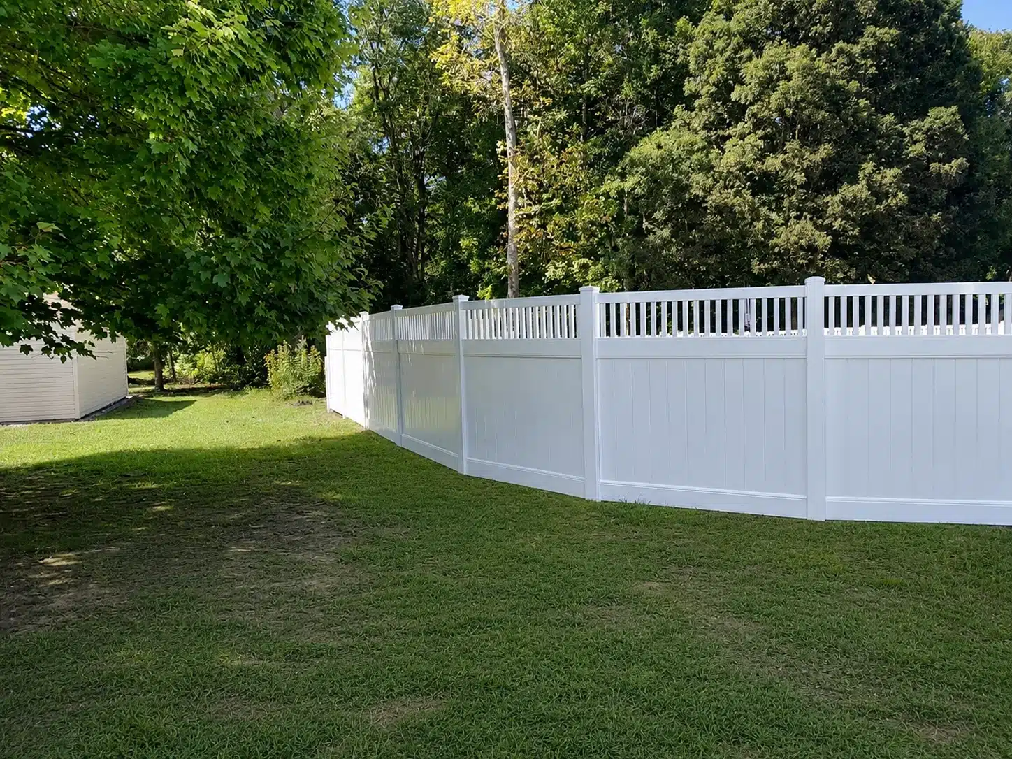 White semi-privacy vinyl fence with narrow picket-top panels installed along a wooded property in Severna Park, MD.