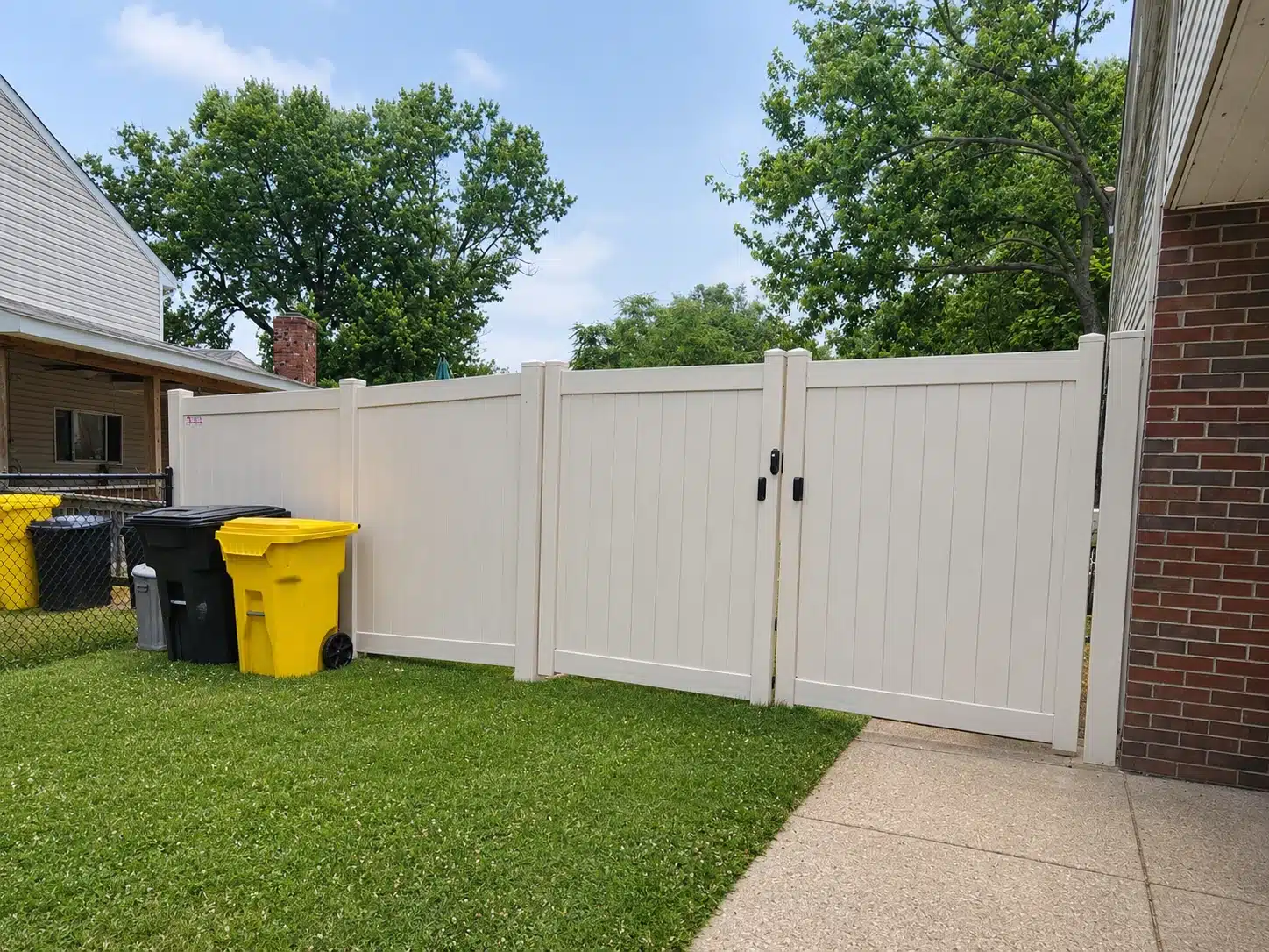 White vinyl privacy fence with a wide double drive gate beside a concrete walkway in Pasadena, MD.