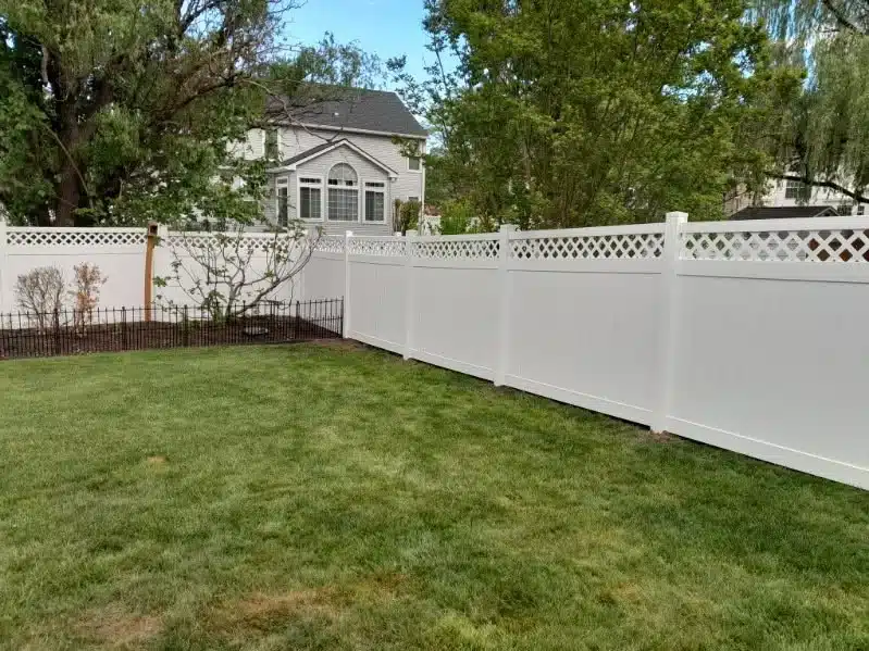 White vinyl privacy fence with a decorative lattice top installed around a landscaped backyard in Pasadena, MD.