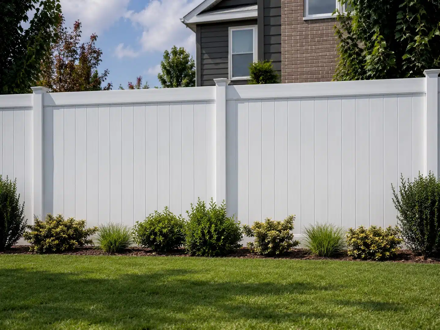 White vinyl privacy fence with full solid panels installed in a landscaped suburban backyard