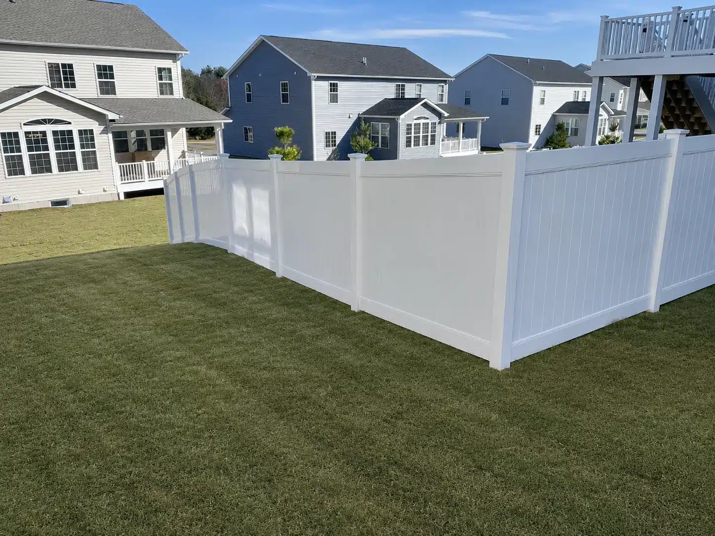 White vinyl privacy fence forming a corner around a sloped backyard in Pasadena, MD.