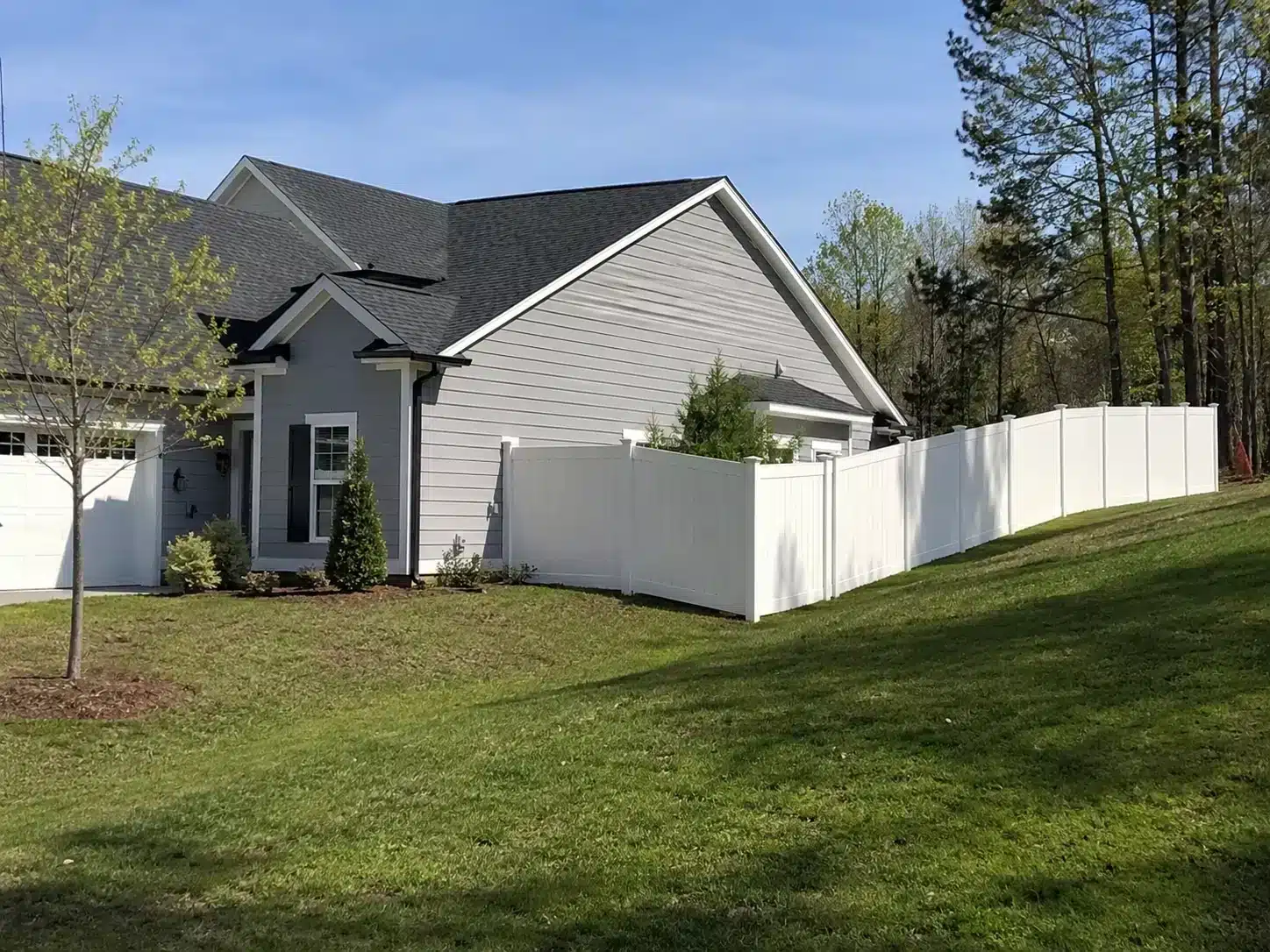 White vinyl privacy fence installed along a sloped residential yard beside a suburban home.