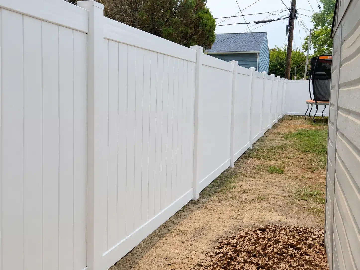 White vinyl privacy fence running through a narrow residential side yard in Pasadena, MD.