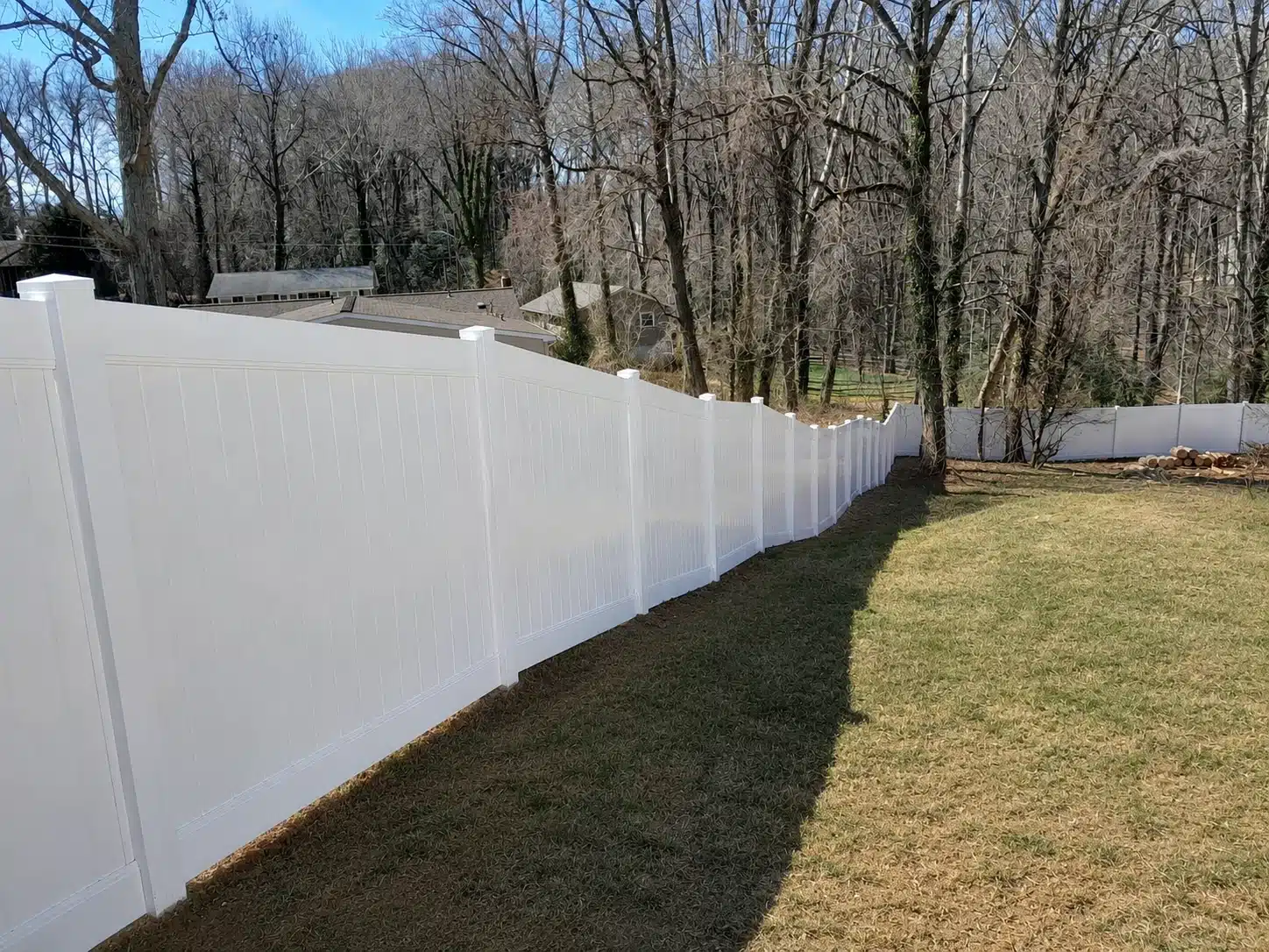 White vinyl privacy fence following the slope of a wooded backyard in Pasadena, MD.