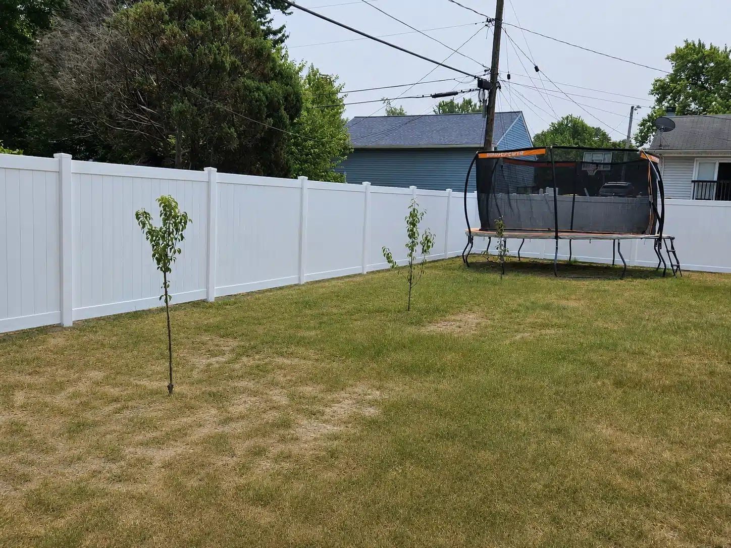 White vinyl privacy fence surrounding a backyard with a trampoline and young trees in Pasadena, MD.