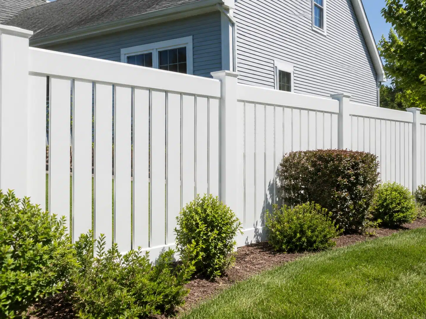 White vinyl privacy fence with solid panels in a landscaped residential backyard